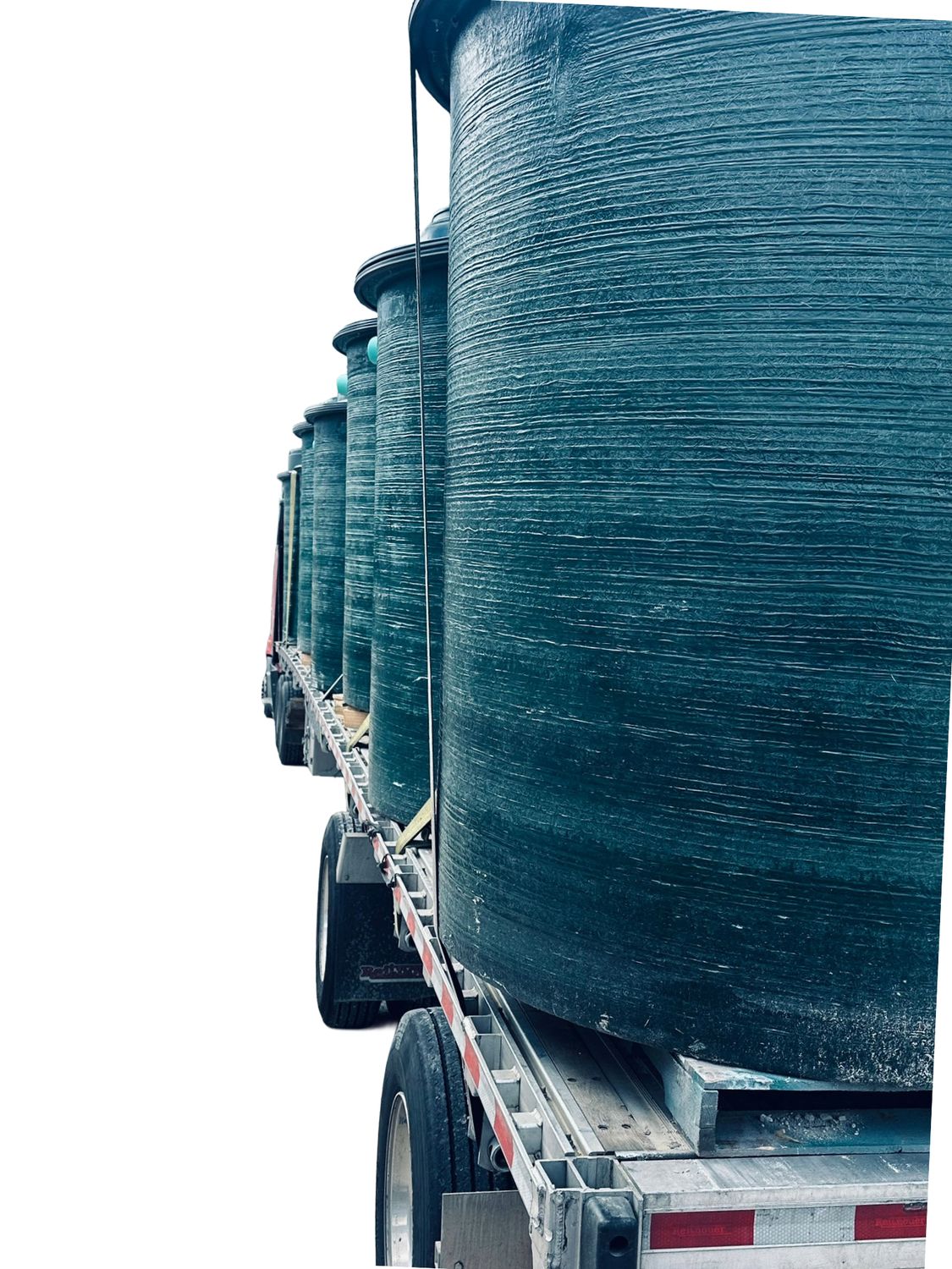 A flatbed loaded with finished fiberglass tanks leaving the yard